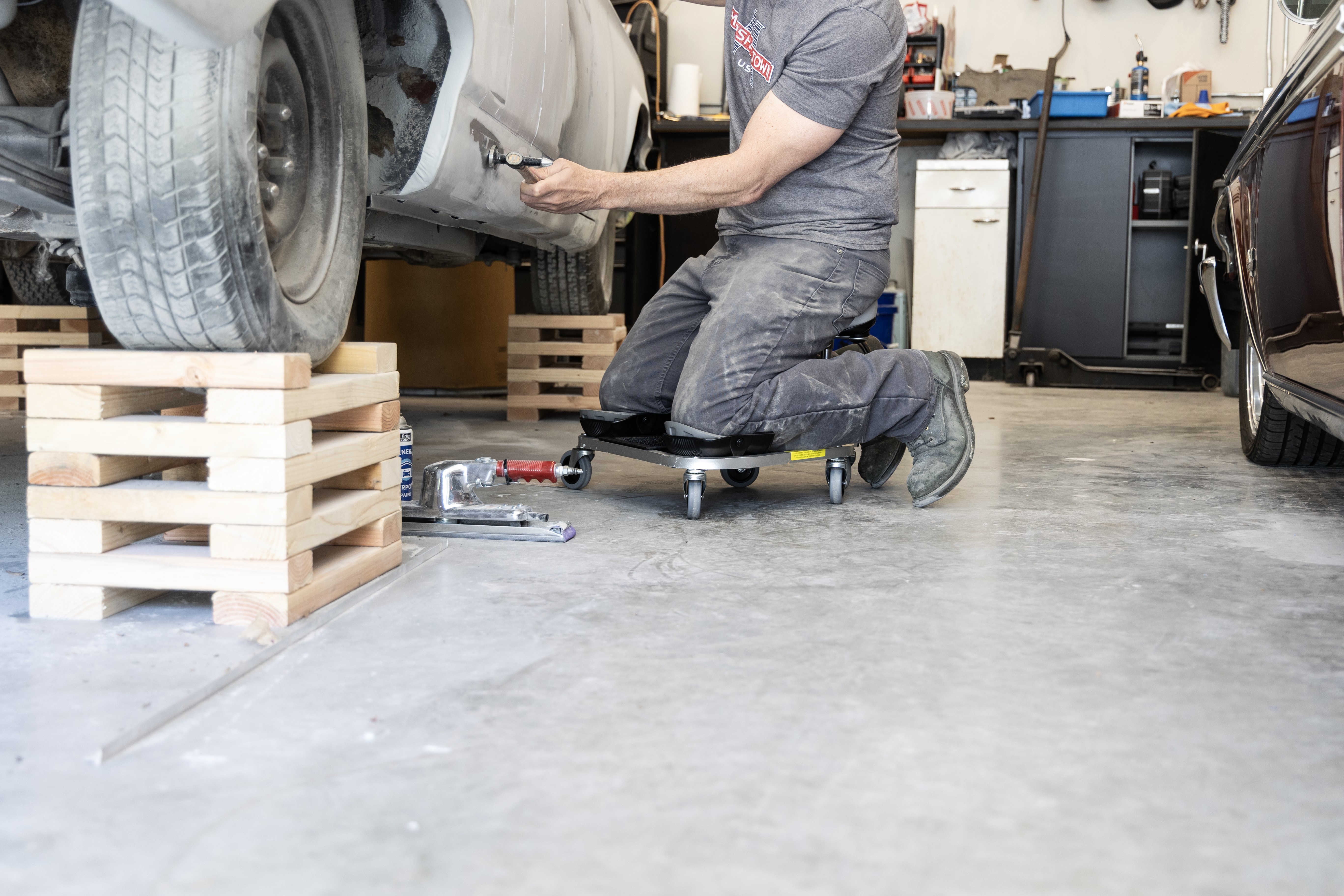 man kneeling on the RACATAC while working on a car